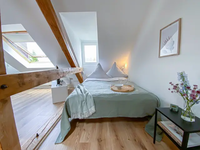 Schlafzimmer mit Doppelbett unter Holzbalken, Über den Dächern